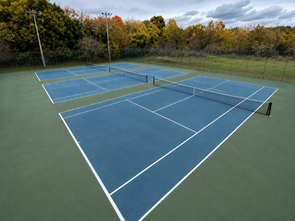 Overhead view of four blue and green pickleball courts at Albion Gardens Park with nets and autumn trees