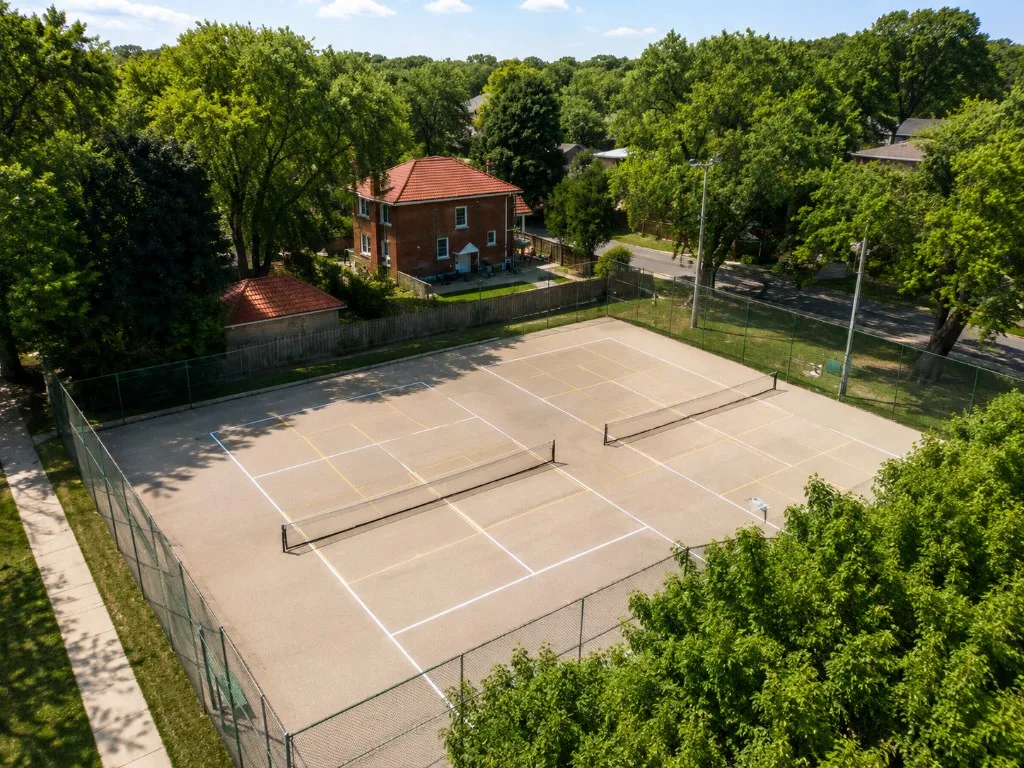 Two fenced outdoor tennis and pickleball courts at Birch Park with yellow lines and light poles