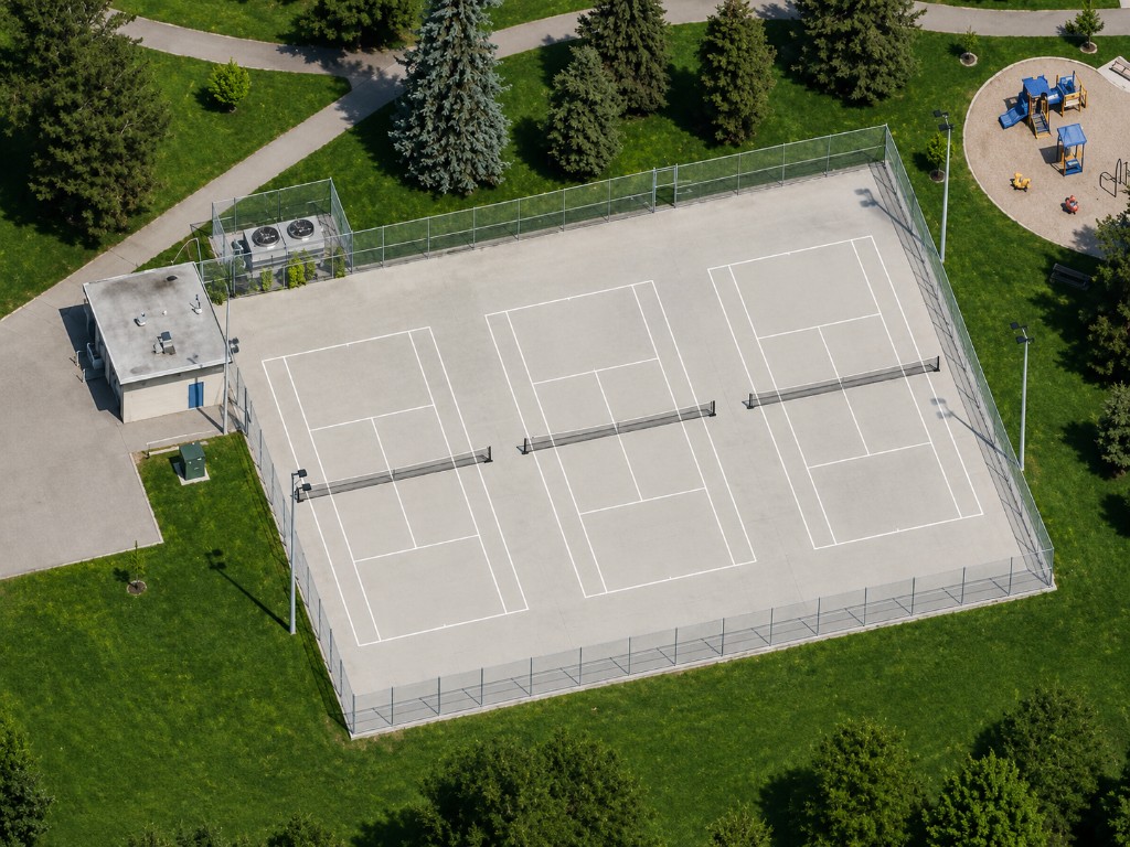 Aerial view of three fenced outdoor tennis and pickleball courts at Buttonwood Park with lights