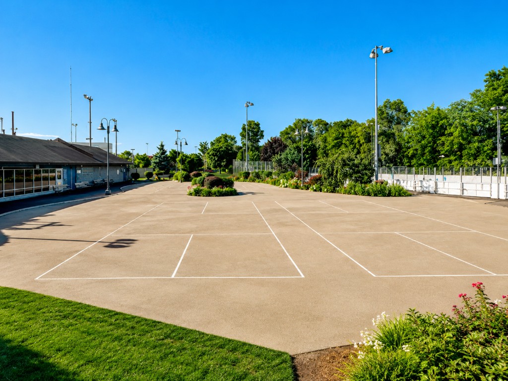 Overview of the tan concrete sports pad with white pickleball lines and light poles at Dieppe Park, East York