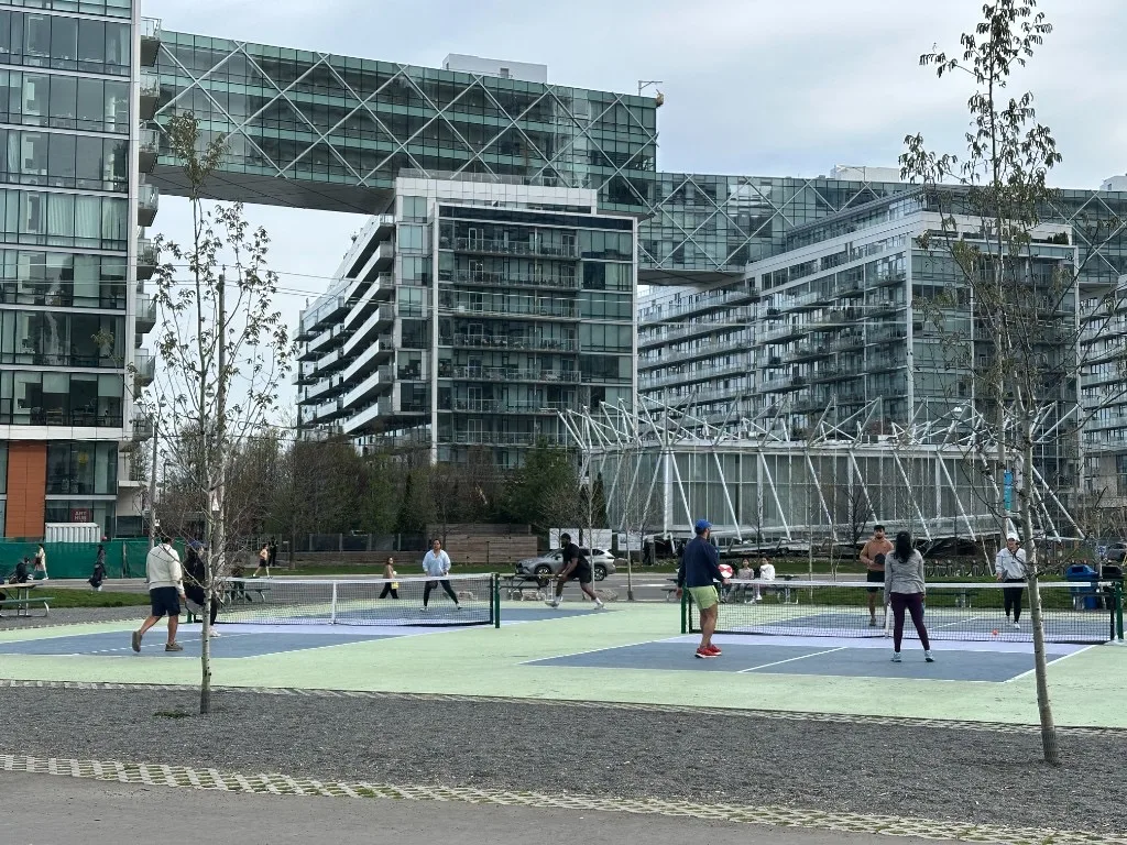 Pickleball courts at 50 Queens Quay East with glass towers and skybridge at One Yonge